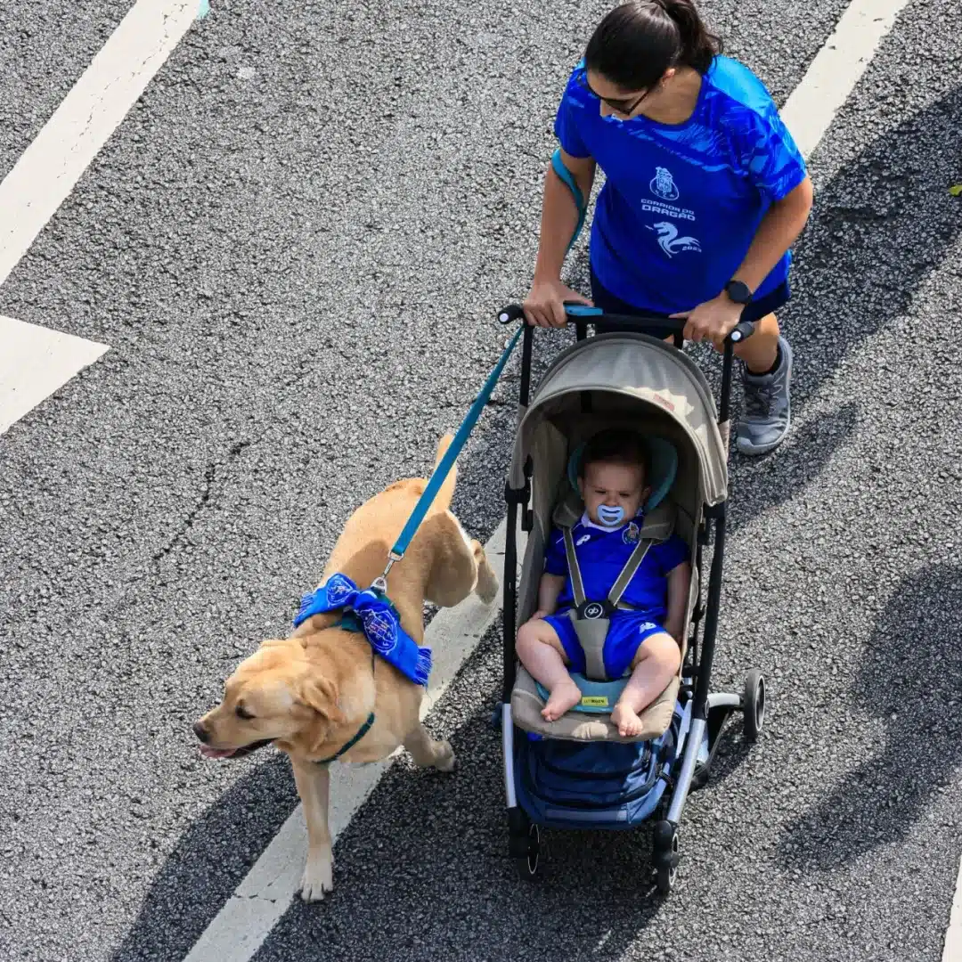 Mulher faz a caminhada da Corrida do Dragão, acompanhada de um cachorro e um bebê no carrinho.