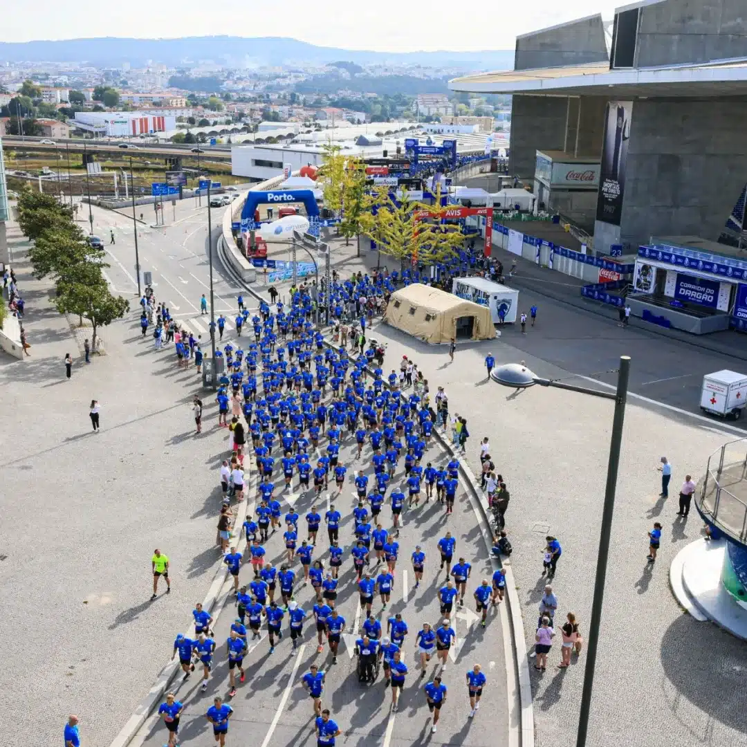 Imagem aérea de um grupo de pessoas correndo, com blusa azul, em um trajeto que forma a letra "S".