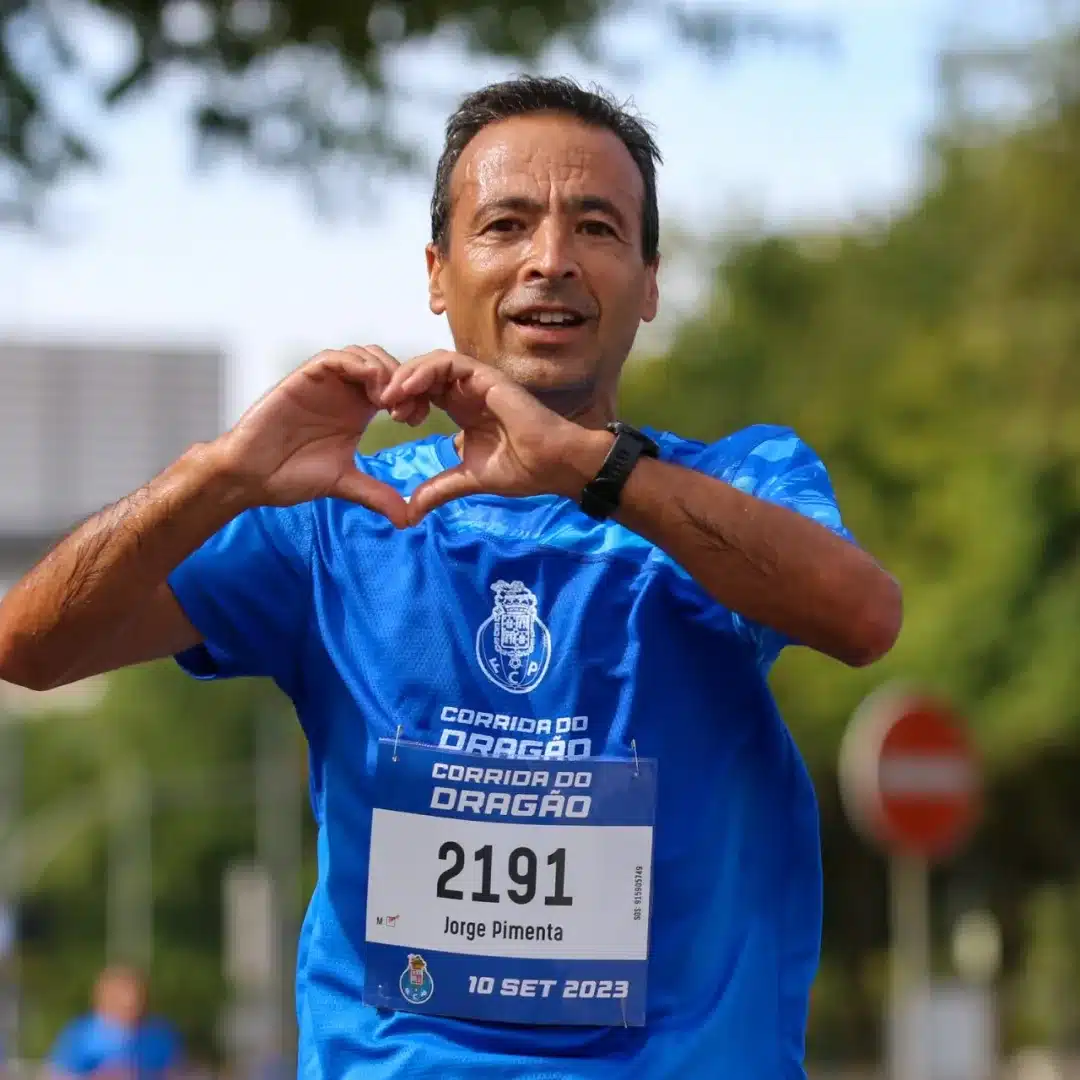 Homem corre olhando para a câmera, fazendo um coração com as duas mãos.