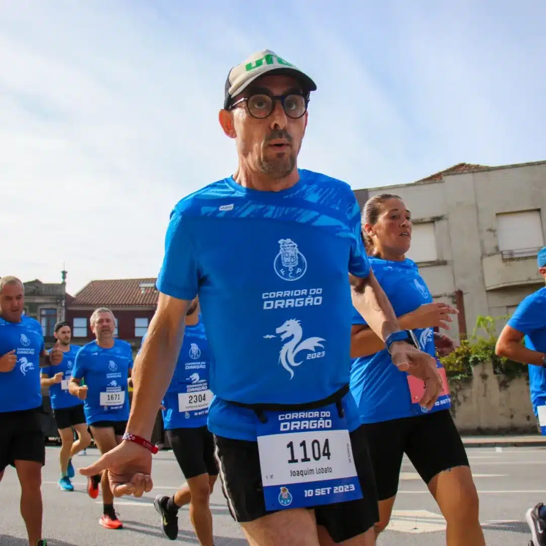 Imagem de um homem com boné respirando fundo durante a corrida, com outras pessoas ao fundo.