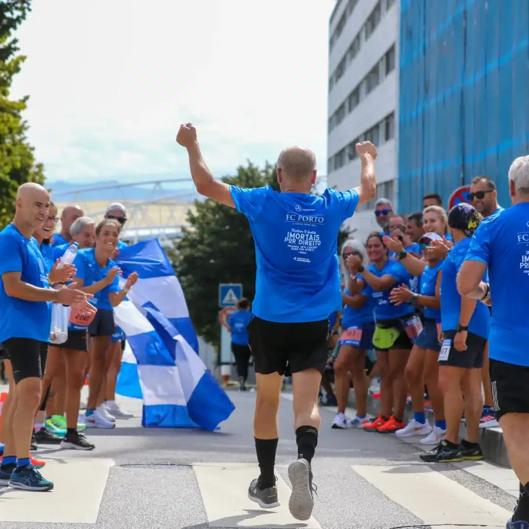 Homem com os braços levantados comemorando, enquanto outras pessoas observam e aplaudem.